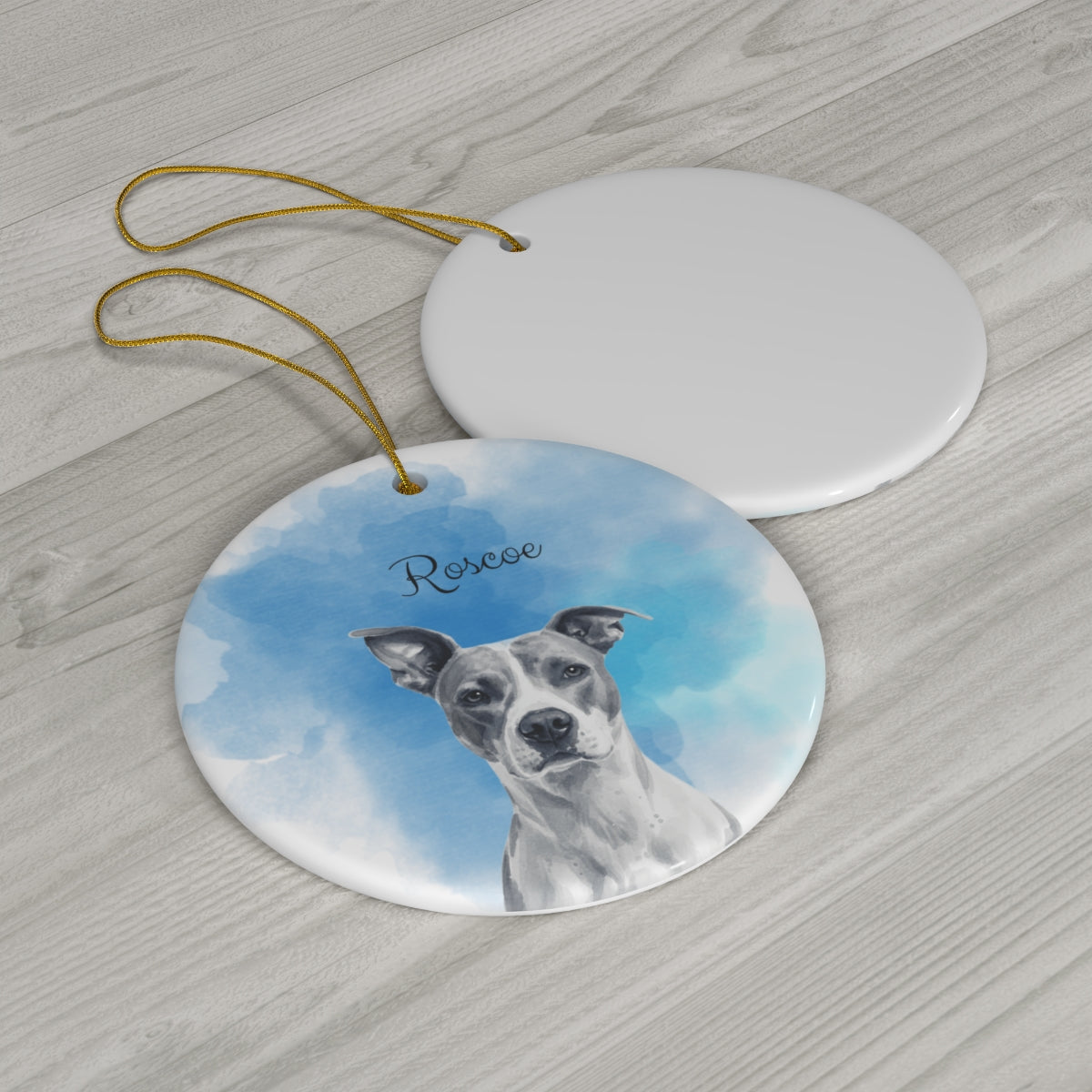 Round ceramic ornament with a dog's face on a blue sky background, placed on a wooden surface.