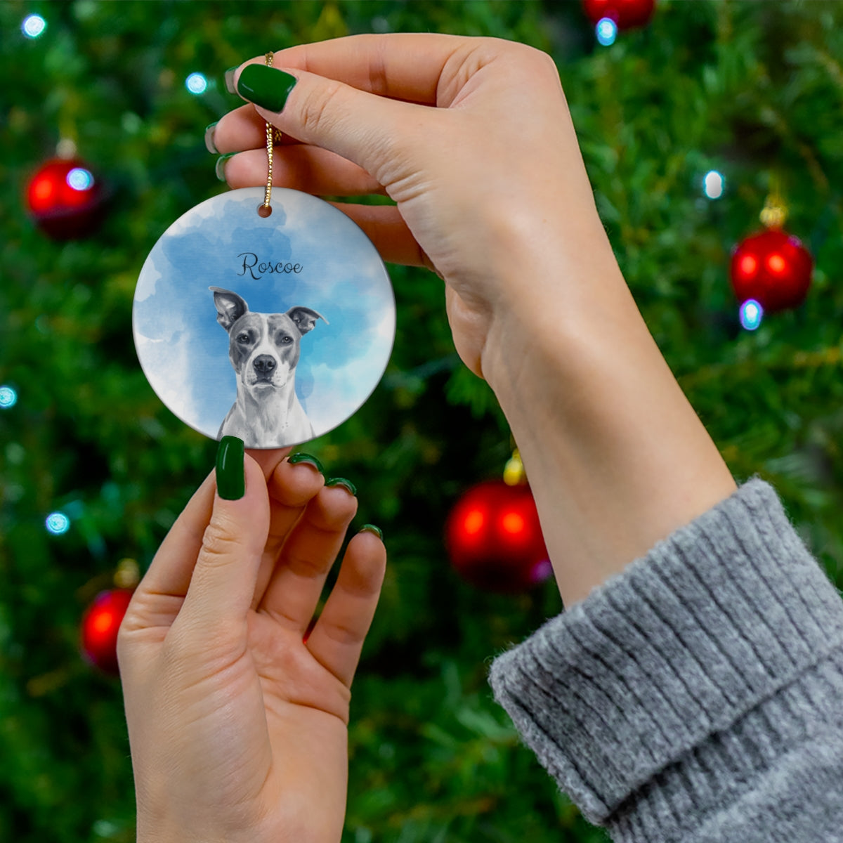Hand holding a pet memorial ornament with a dog's face on a Christmas tree background